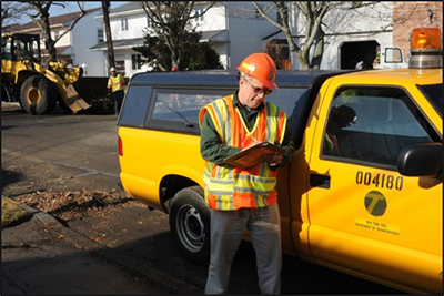 man wearing safety vest writing on clipboard. He is standing outside of a truck.