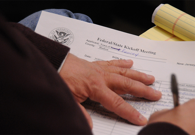 Writing name on sign-in sheet at a Public Assistance Kick-Off Meeting