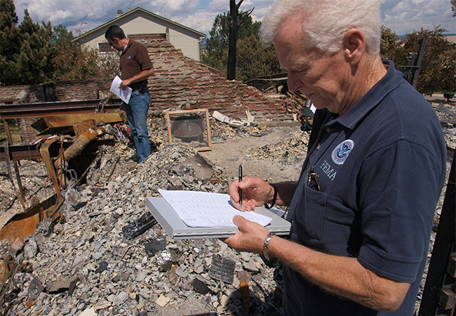 FEMA representative works with the joint Preliminary Damage Team to assess damage on the remains of a destroyed building.