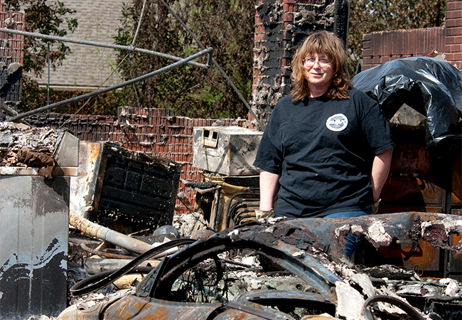 Woman overlooks debris from a home and a vehicle severely damaged in a wildfire.