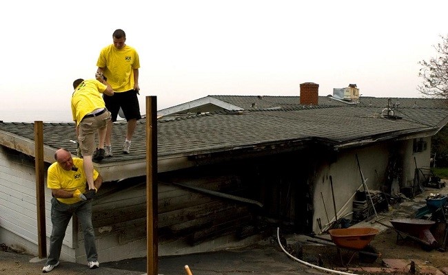 Three volunteers climb on a home to help clean up and remove debris following the 2007 Malibu Canyon fire.