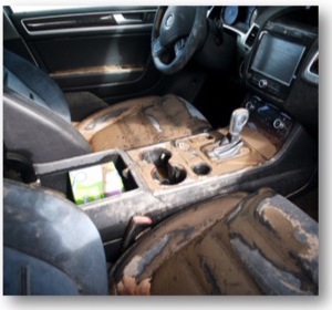 A photo of the interior of a flood-damaged vehicle. The front seats and the middle console are covered in dried mud.