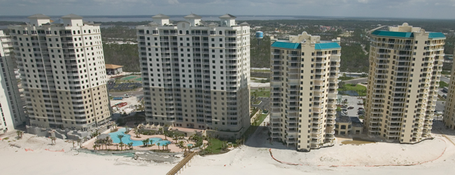 An aerial photograph of four large condominium buildings near a beach.