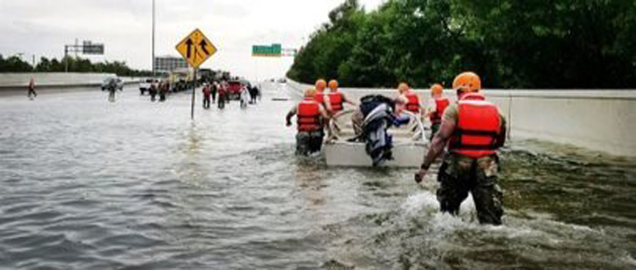 A group of rescue workers walking with a boat in a flooded street.