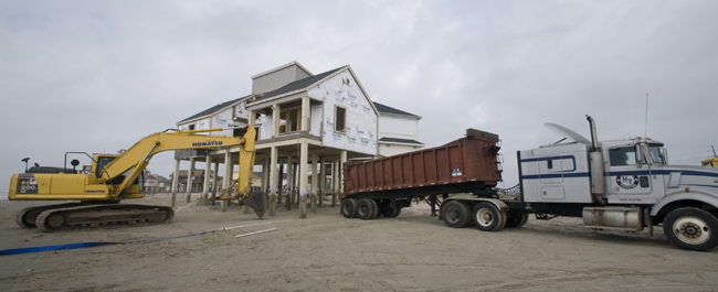 A house in the process of being elevated with an escavator and tractor trailer in front. 