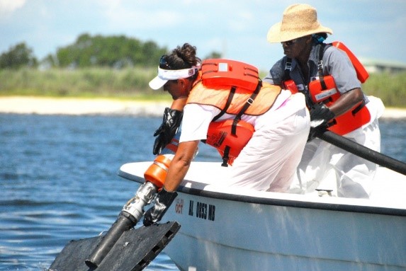 Two people on a boat pulling equipment out of the water.