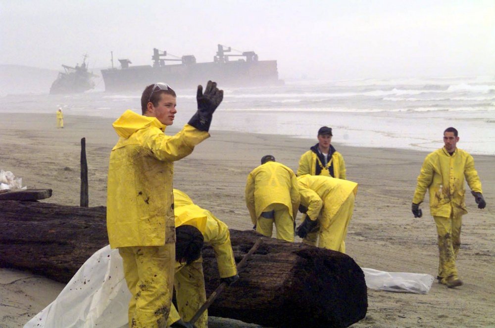 Responders cleaning up the oil spill on the Oregon shoreline. The New Carrisa oil tanker can be seen in the water in the background.