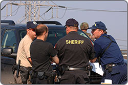 Image of law enforcement officials collaborating. The back of one officer’s shirt reads “SHERIFF.”